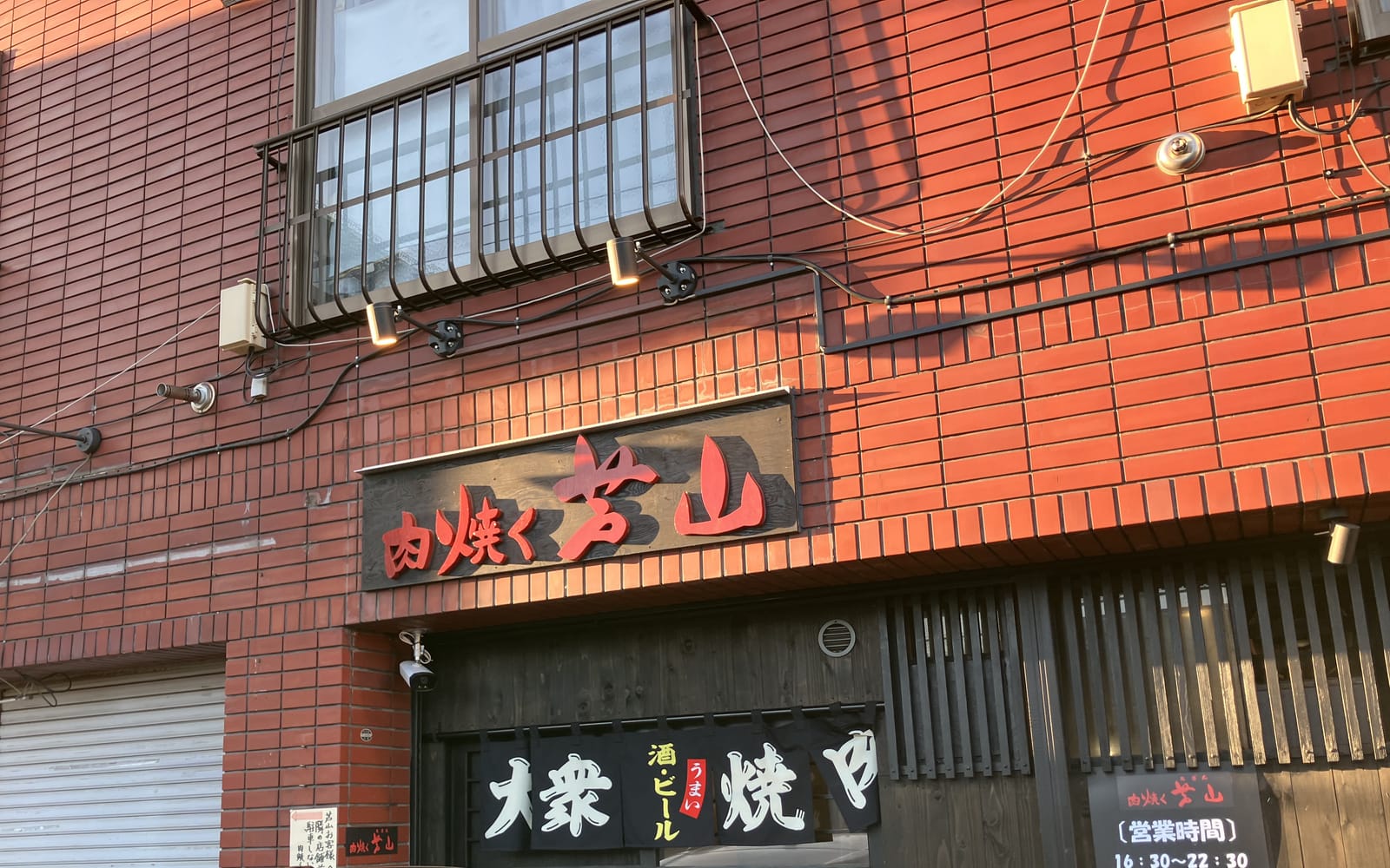 外観。赤いレンガの建物1階、「肉焼く 芦山」の看板と大衆焼肉の暖簾